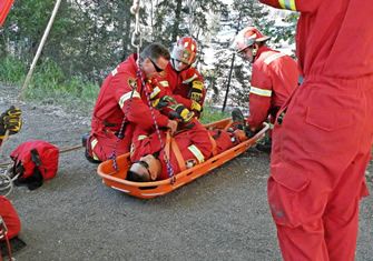 Rescuers in red coveralls moving a patient on a stretcher up an embankment